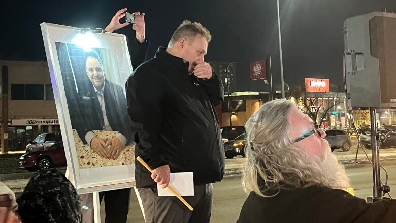 A man stands beside a picture of another man.