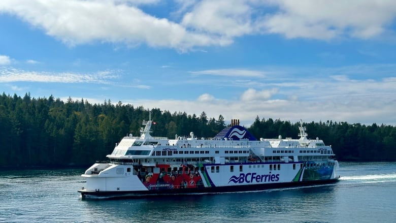 A large passenger ship sails through the water, with trees and blue sky behind it. 