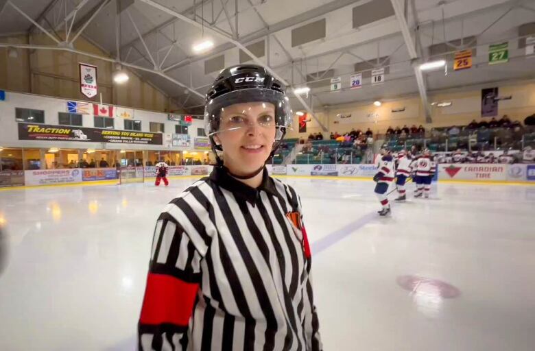 A woman wearing a referee's uniform smiles on the ice.