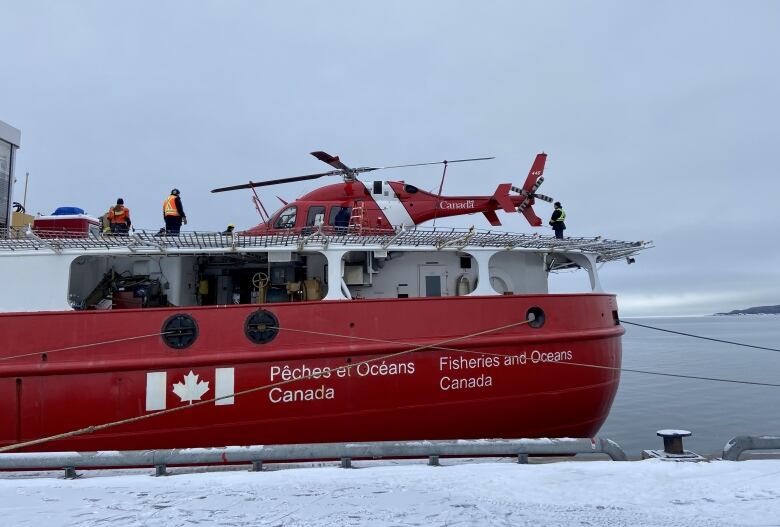 The stern of a Fisheries and Oceans Canada vessel docked with a helicopter and crew on the deck.