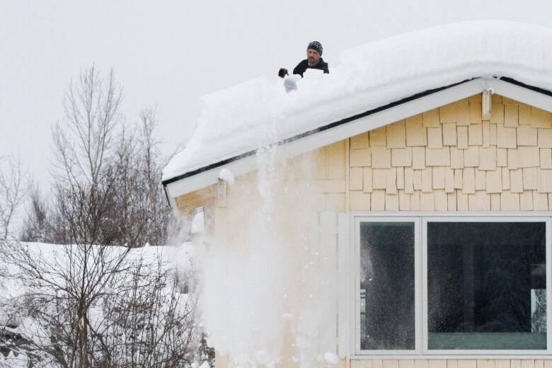 A man shovels snow off the roof of a house.