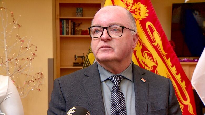 Man with glasses standing in front of a yellow and red flag. 