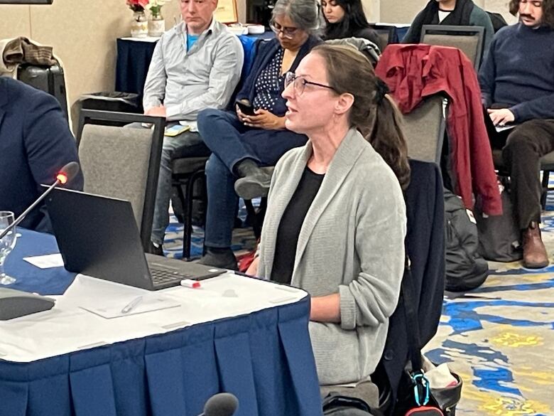 A woman with glasses sitting next to a table with a laptop on it.