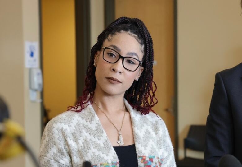 a woman wearing glasses looks at the camera. She is standing in front of microphones. 