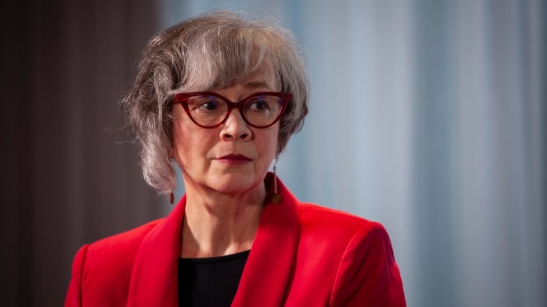 A woman in a red coat and a winged pair of glasses is pictured during a news conference.