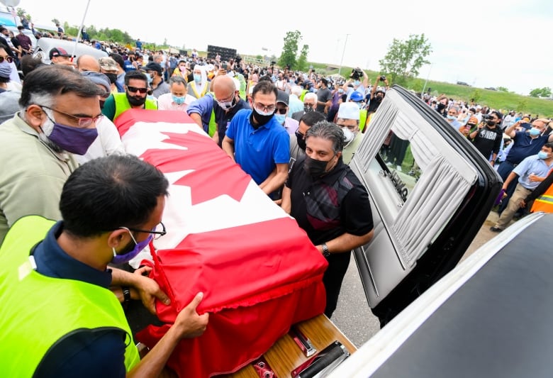 Pallbearers carry a coffin covered by a Canadian flag.