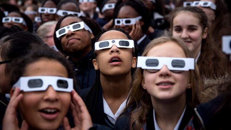 Group of awed children wearing protective eclipse glasses and staring at the sky.