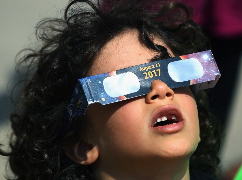 A child looks up wearing disposable eclipse glasses with 2017 written on them.