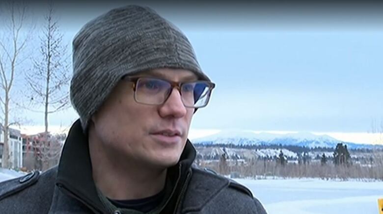 Portrait shot of a man in a grey toque and glasses, standing on an icy landscape. 