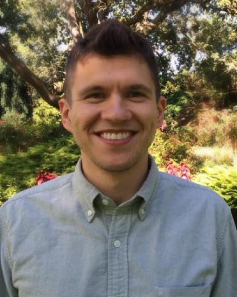 Gleb Glebov, a smiling man with short brown hair wearing a blue collared shirt, stands in front of a garden.