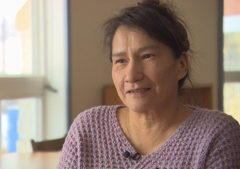 A First Nations woman is wearing a lavender sweater and smiling.