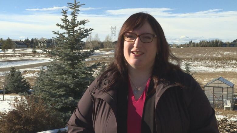 a woman with glasses stands outside.