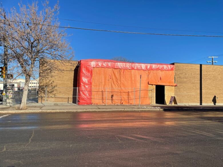 A brown building on a street in Regina is covered in orange tarp. This building is the future home of the Regina Food Bank's Community Food Hub. 