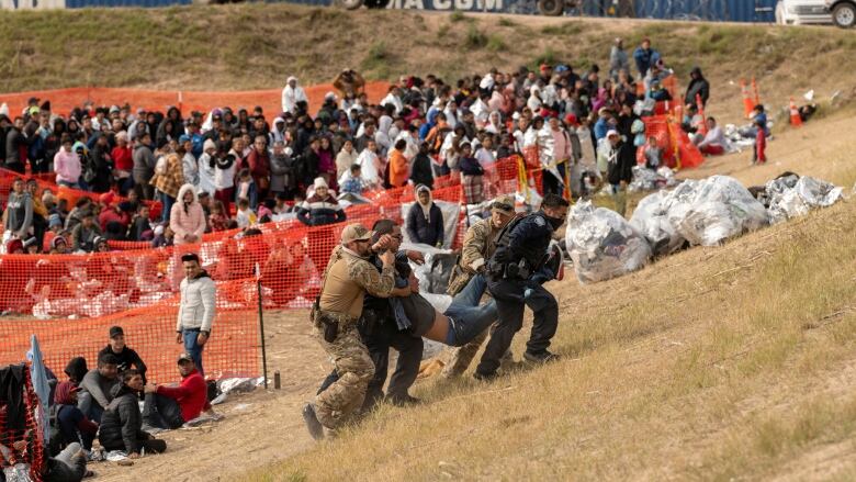 At an outdoor processing centre for migrants at Eagle Pass, Tex., federal and state officers carry a migrant with a medical emergency out of a crowd.