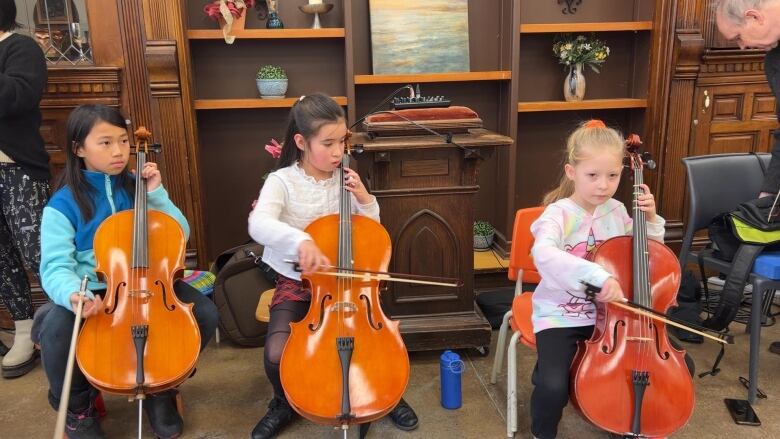 Three children sit with cellos in hand.