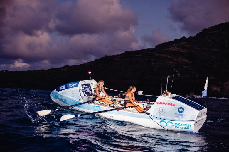 Two women row a blue and white open water boat