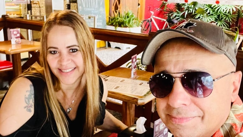 A man and a woman smile while seated at a cafe table.