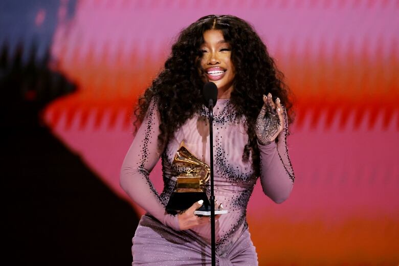 A woman wearing a purple dress with sequins holds a Grammy award.