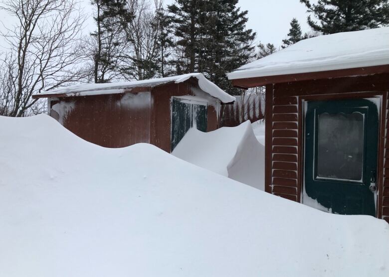 Snow drifts up against a red building.