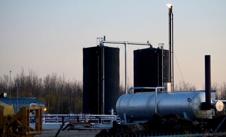 Natural gas pipes and tanks are seen with a forest in the background.