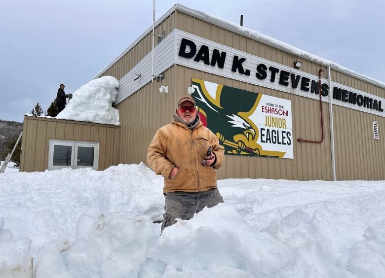 A man is shown in deep snow beside building that houses a hockey arena.