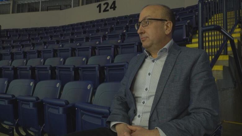 Man in a suit sitting in an empty hockey stadium. 