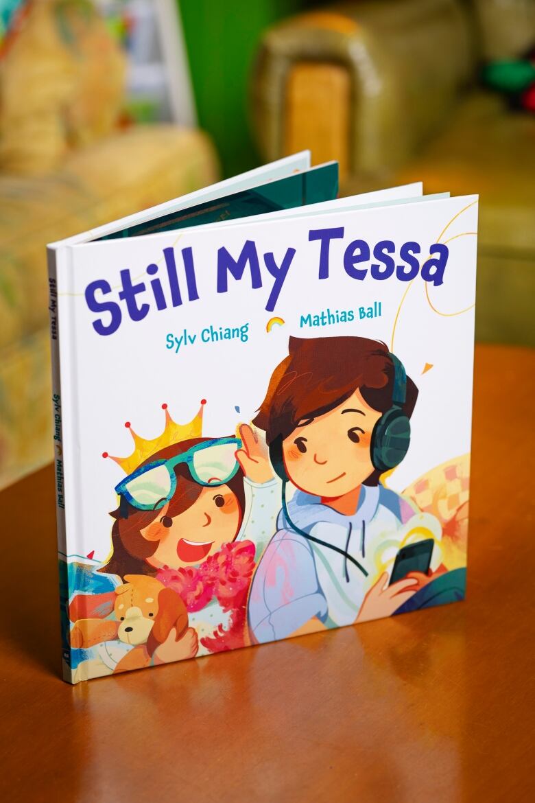 A picture book with a cover showing two children, one wearing a crown and sunglasses and the other wearing headphones attached to their phone. 