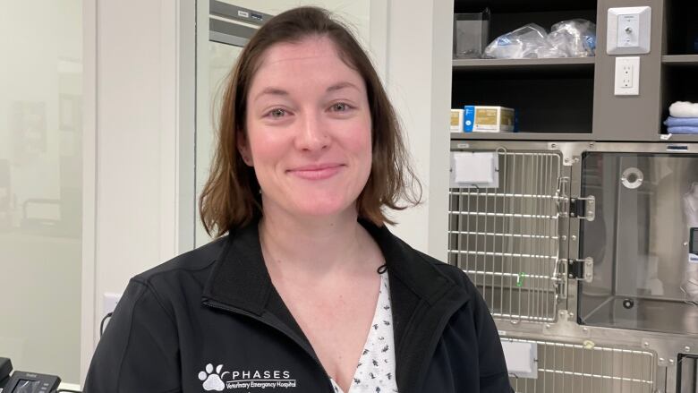 Smiling woman with shorter brown hair stands in front of metal animal cages in a vet office