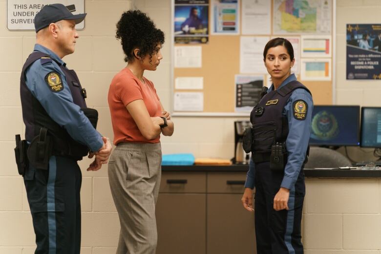 Two police officers stand around a woman with crossed arms. 