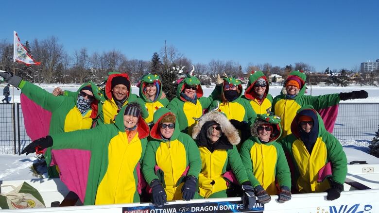 A team of people wearing dragon onesies outside in the winter. 