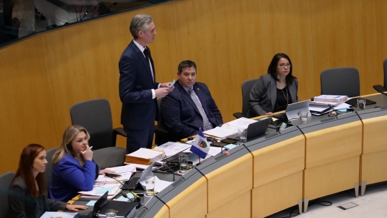 Man in suit stands in legislative assembly.