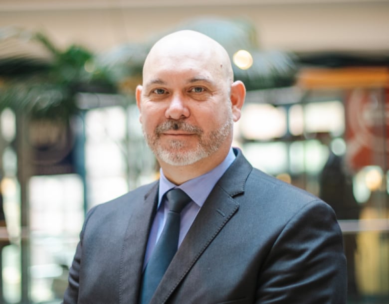 Man in a suit looks gravely into camera.