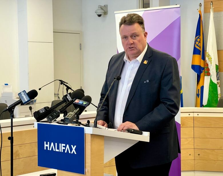 A man in a suit with a white dress shirt stands in front of a podium. It reads: Halifax.