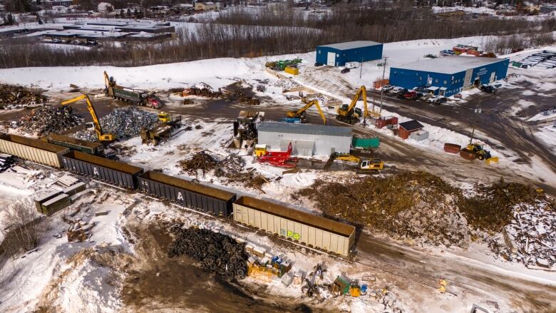 Empty train cars with piles of scrap material and several buildings.