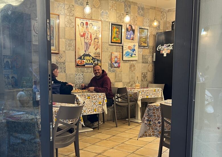 A man and a woman sit at a table in a small restaurant eating pizza. 