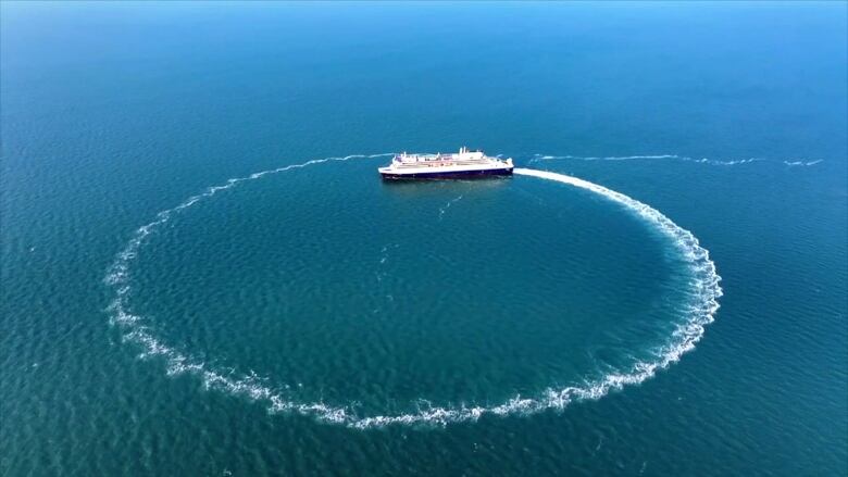 A large ferry drives in a circle on a blue ocean, making a circle wake. 