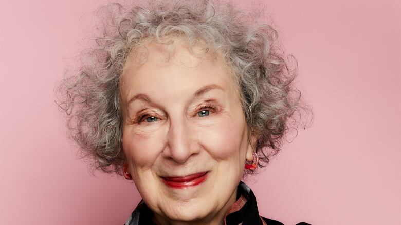 A woman with curly grey hair and wearing pink lipstick smiles at the camera. 