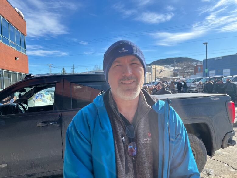 Man in blue winter jacket with truck behind him