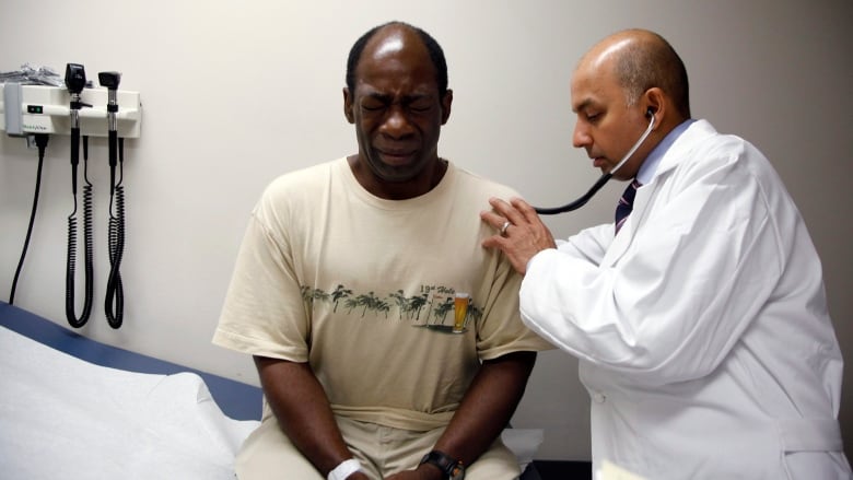 A man winces as a doctor examines him with a stethoscope.