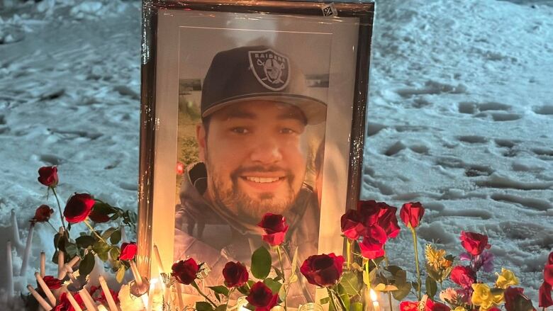 Roses and candles sit front of a framed photo of a man with a beard and black baseball cap.