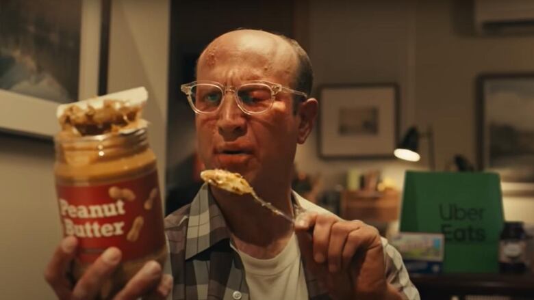 A man with a swollen eye and hives breaking out on his forward reads the label of a peanut butter jar. 