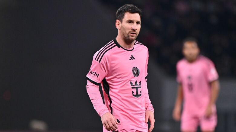 Men's soccer player stands on a soccer pitch.