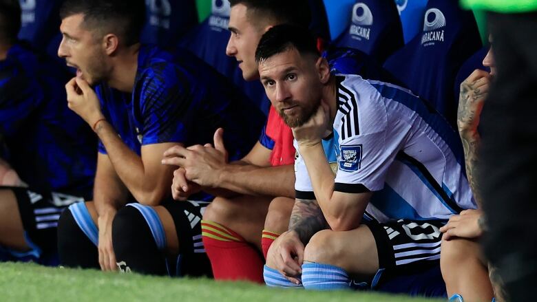 Argentinian men's soccer player looks on from the bench while sitting down.