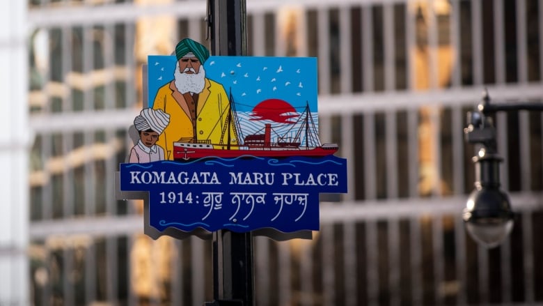 A blue sign showing a Sikh man and boy on a stylized ship in a waterfront sits on a pole, with the words 'Komagata Maru Place' on it.