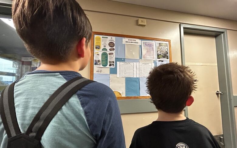 Two youths looking at a notice board.