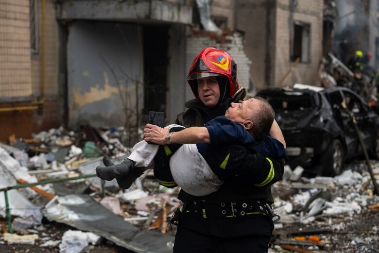 A firefighter carries a wounded man in front of a backdrop of rubble.