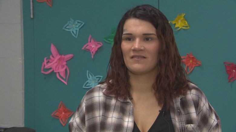 A woman with brown hair, wearing a plaid shirt, is looking off camera.