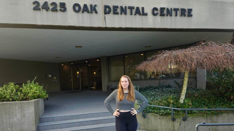 A woman in leggings and a top stands outside a dental centre. 