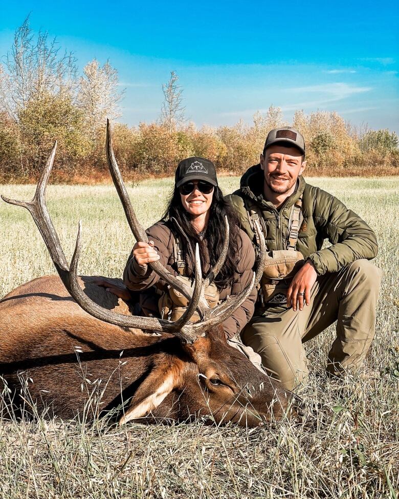 A couple in camo over a dead elk.