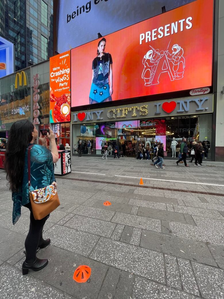 A woman takes a photo of a large billboard depicting an Inuk model wearing a fashionable dress.